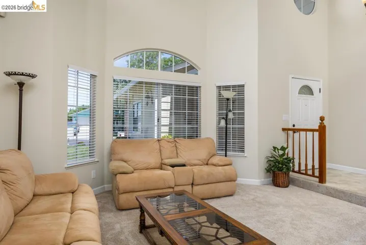 Vaulted ceilings defining a spacious living area featuring multiple windows with blinds, an arched transom window, and neutral-toned wall paint