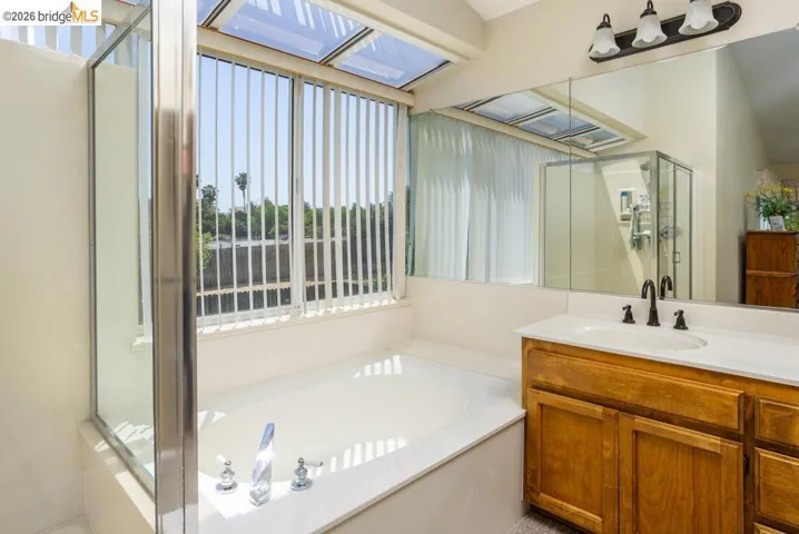 Bathroom featuring a soaking tub, glass-enclosed shower, and a wood-finish vanity with a white countertop