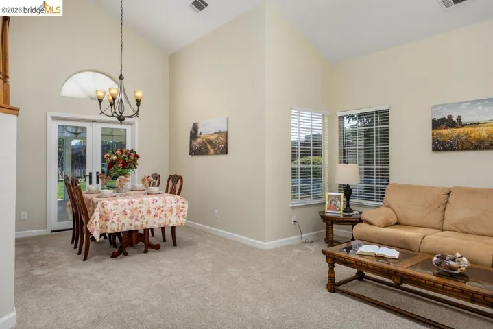Vaulted ceilings define this carpeted interior featuring a dining area with a wrought iron chandelier and double glass doors