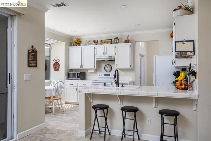 Kitchen featuring white cabinetry, tile countertops, recessed lighting, and a breakfast bar