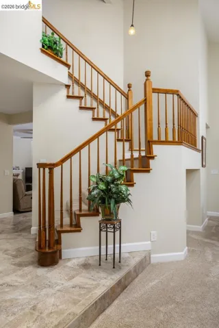 Two-story foyer featuring a wood staircase with turned balusters, light beige wall paint, and a combination of carpet and stone-finish tile flooring