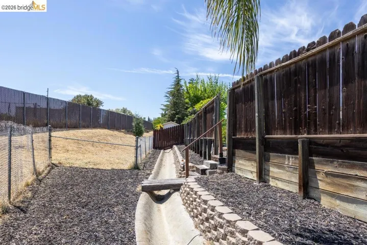 Tiered backyard area featuring a concrete channel, wood privacy fencing, and chain link fencing