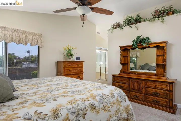 Carpeted room featuring a vaulted ceiling with a ceiling fan, a window with a valance, and an architectural ledge