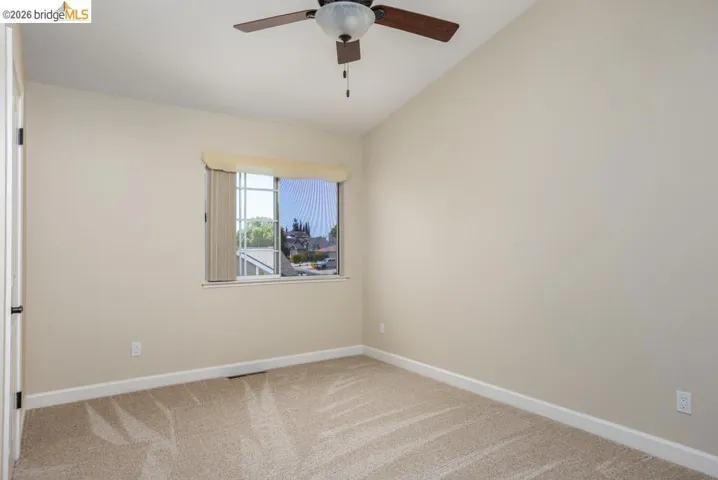 Carpeted room featuring a window with vertical blinds, a ceiling fan with integrated lighting, and a vaulted ceiling