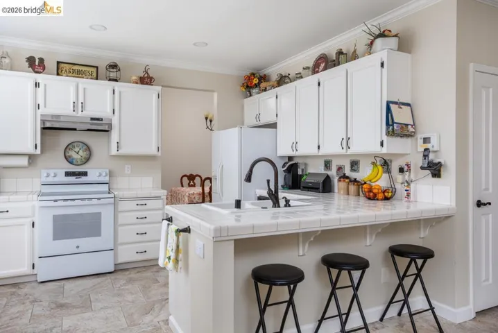 Kitchen featuring white cabinetry, tile countertops, a white appliance suite, black hardware, and tile flooring