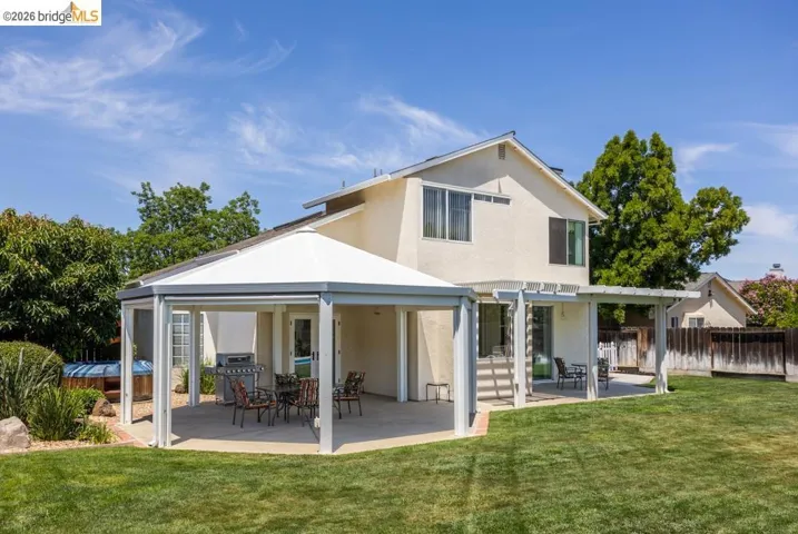 Expansive backyard with a manicured lawn, featuring a covered patio with an octagonal gazebo and an additional pergola-covered concrete patio area