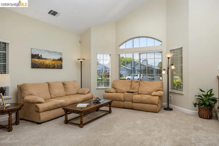 Living area featuring vaulted ceilings, a large arched window with blinds, and light-toned carpet flooring
