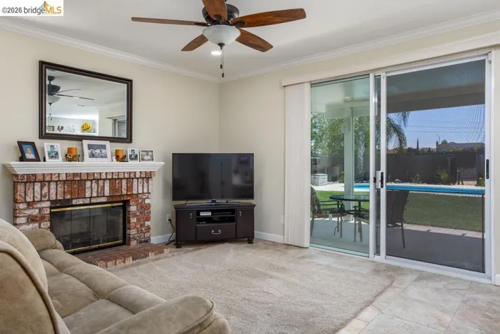 Living area featuring a brick fireplace with a white mantle, ceiling fan, and crown molding