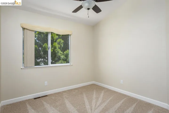 Vaulted ceiling room featuring a ceiling fan with light, a window with exterior tree-line scenery, neutral carpet flooring, and baseboard trim