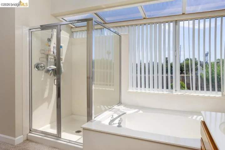 Full bathroom featuring a walk-in shower with clear glass enclosure, a built-in bathtub with deck-mounted fixtures, and a large window with vertical blinds