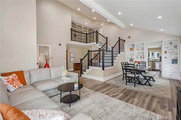 Living room including vaulted ceiling, recessed lighting and view into dining room area including built ins at Kitchen entry and staircase leading to upstairs area.