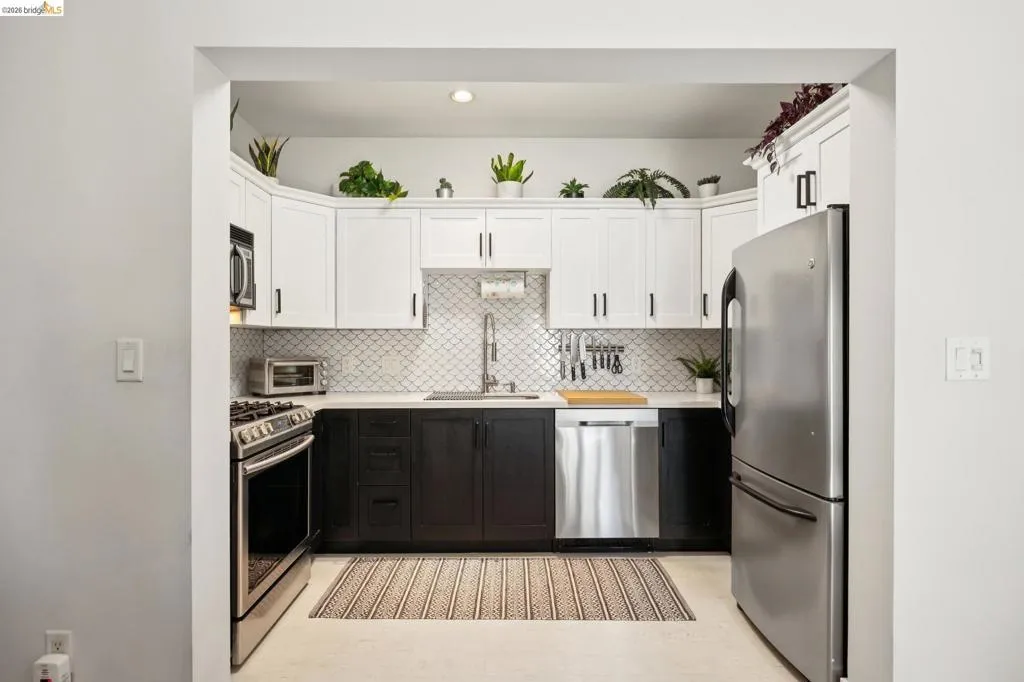 Kitchen featuring stainless steel appliances, two-tone cabinetry with black lower and white upper cabinets, quartz countertops, and a decorative tile backsplash