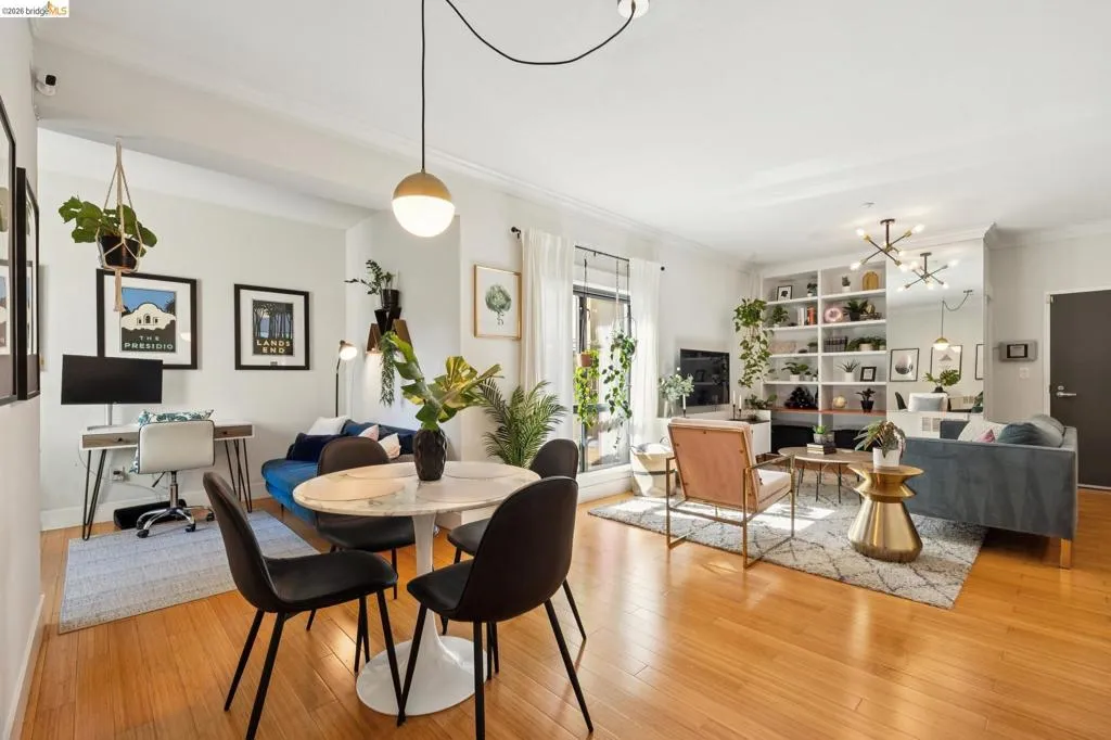 Open-concept living area featuring wood-finish flooring, a built-in shelving unit, a large window, a dining area with a round table, and a dedicated desk space