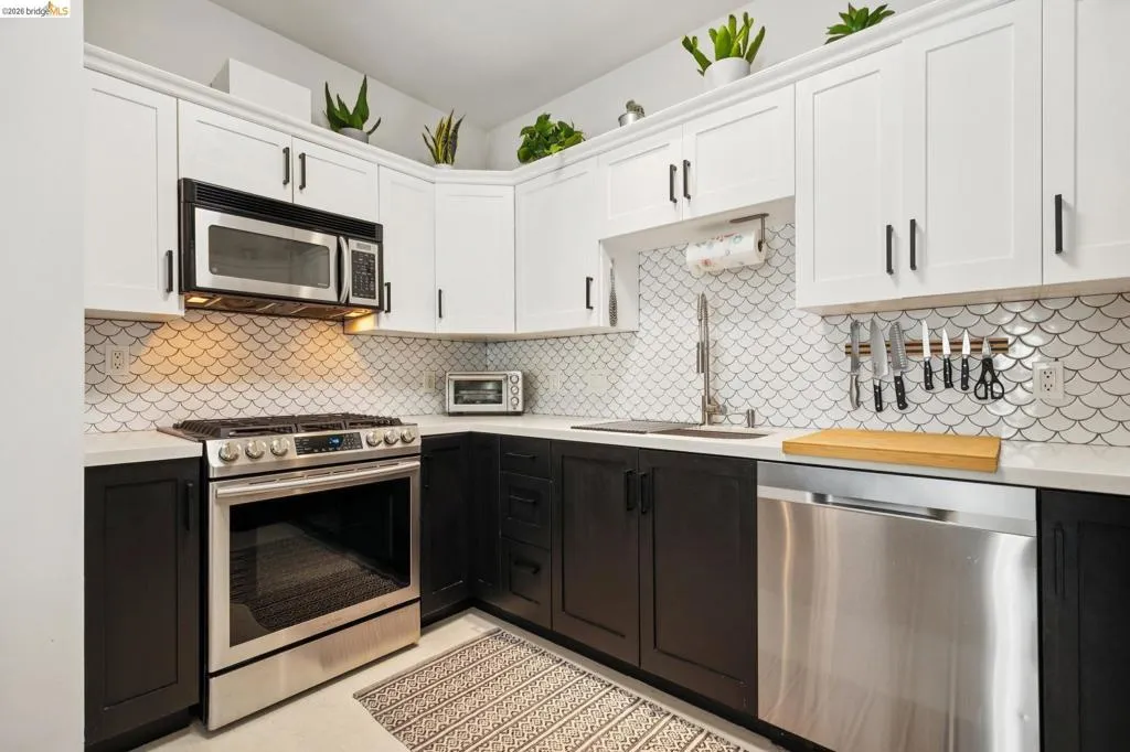 Modern kitchen featuring two-tone cabinetry, stainless steel appliances, a unique scale-patterned tile backsplash, white countertops, and recessed lighting