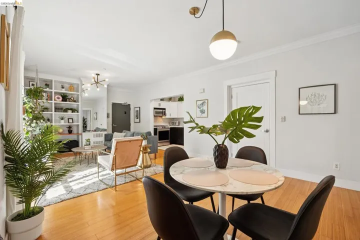 Open-concept living space featuring wood-finish flooring, built-in shelving, a kitchen with stainless steel appliances, and a dining area with a modern pendant light