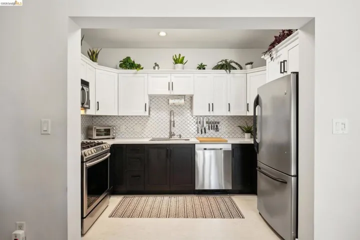 Kitchen featuring stainless steel appliances, two-tone cabinetry with black lower and white upper cabinets, quartz countertops, and a decorative tile backsplash