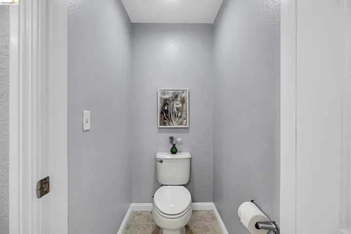 Powder room featuring a commode with a ceramic tank and bowl, light gray textured walls, white baseboards, and tile flooring
