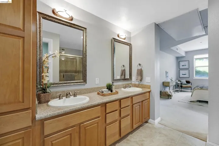 Dual vanity with light wood cabinetry, a light speckled countertop, and two framed mirrors