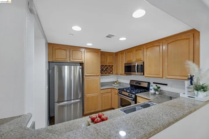 Kitchen featuring granite countertops, wood cabinetry, stainless steel appliances, and recessed lighting