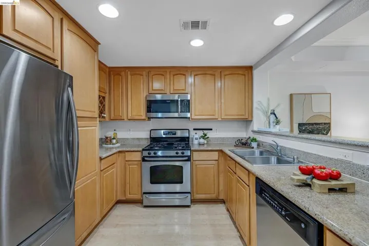 U-shaped kitchen featuring light wood cabinetry, stainless steel appliances, speckled countertops, and recessed lighting