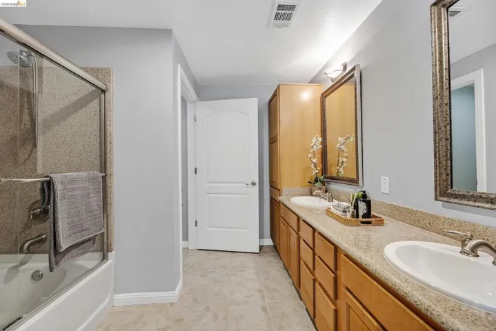 Dual vanity with light wood cabinetry, white sinks, and speckled countertops