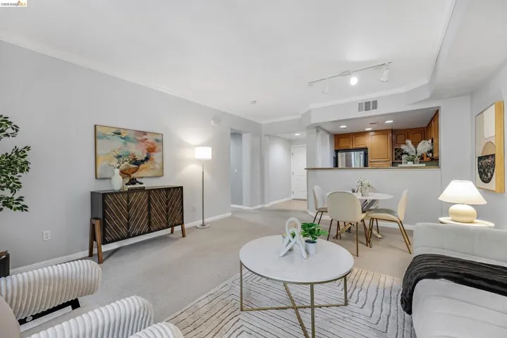 Open-concept living area featuring a carpeted floor, white crown molding, and a partial wall separating the kitchen