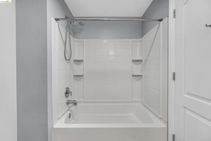 White bath and shower combination unit featuring an integrated soap dish and shelving