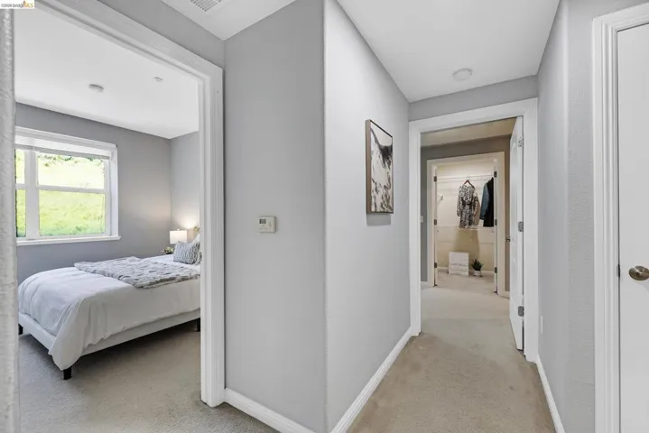Hallway with neutral carpeting and light gray walls, featuring white trim and doors