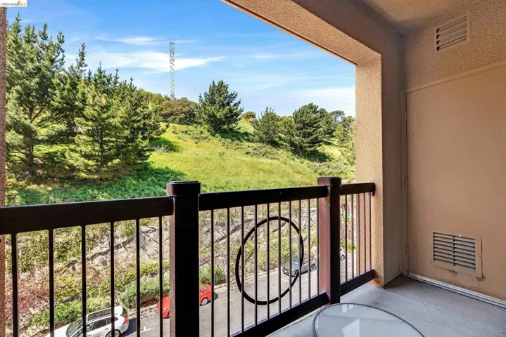 Private balcony with black wrought iron railing and wood-tone posts, featuring a natural hillside backdrop with mature trees and green foliage