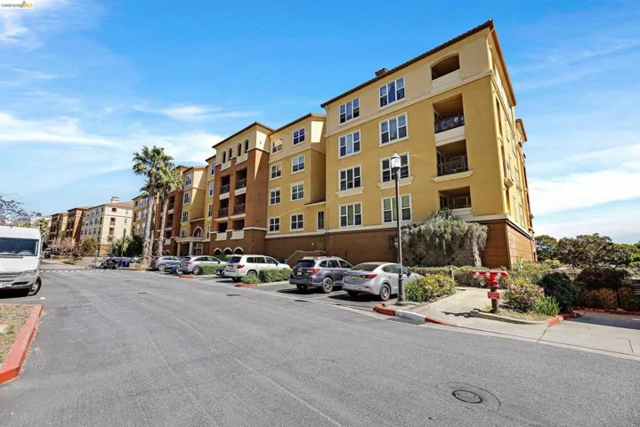 Multi-story residential building featuring a stucco exterior with decorative architectural elements, multiple private balconies, and an established landscape
