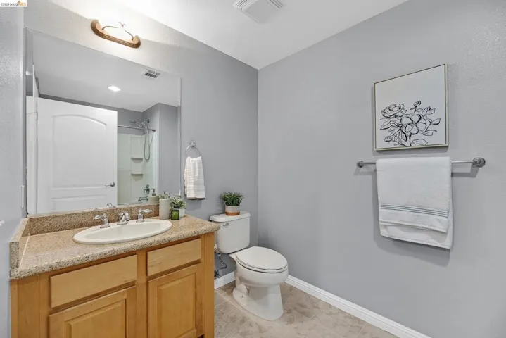 Bathroom featuring a light wood-finish vanity with a stone-finish countertop, undermount sink, and chrome fixtures