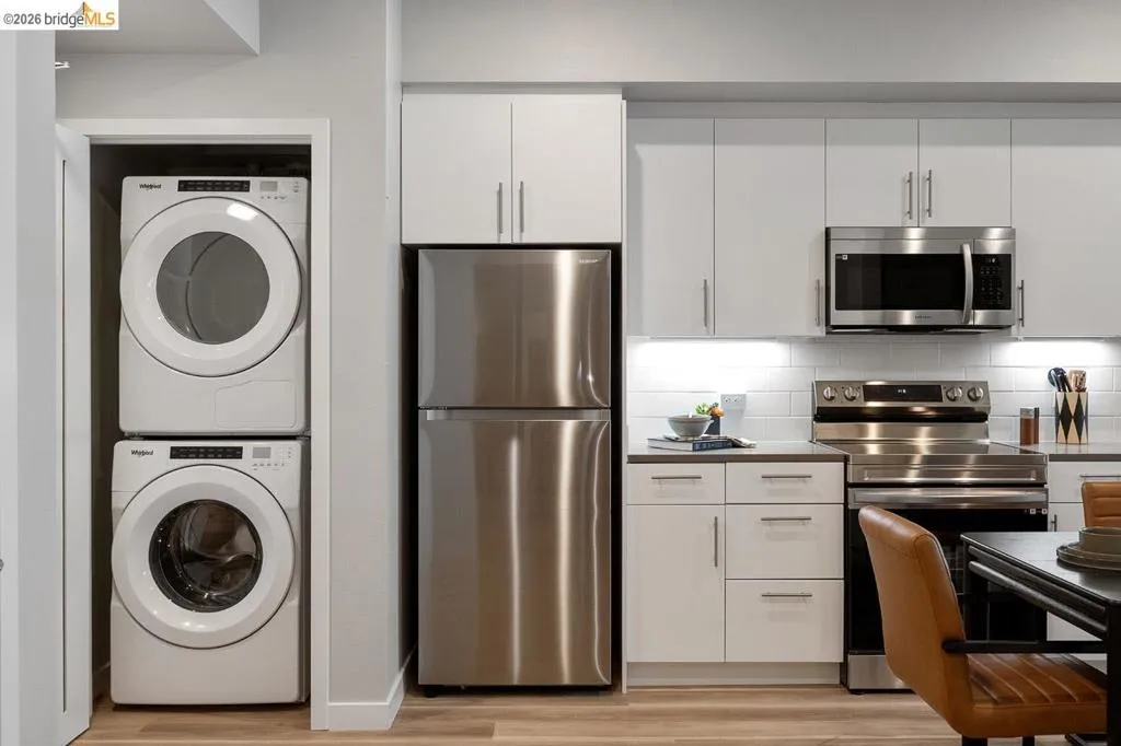 Kitchen featuring stainless steel appliances, white cabinetry, stacked washer and clothes dryer, backsplash, and light wood-style floors