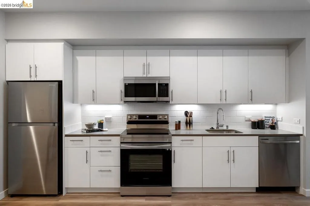 Kitchen with stainless steel appliances, white cabinetry, tasteful backsplash, and light wood finished floors