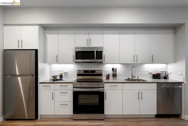 Kitchen with stainless steel appliances, white cabinetry, tasteful backsplash, and light wood finished floors