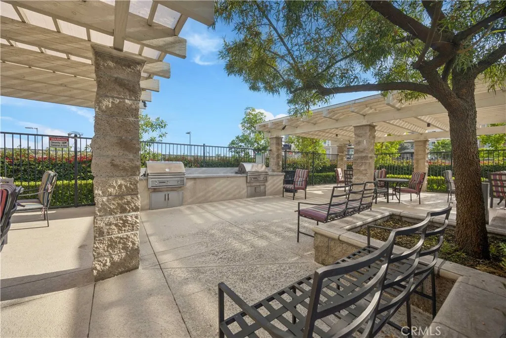 Community outdoor BBQ and lounge area with stone pergola, built-in grills & shaded gathering space.