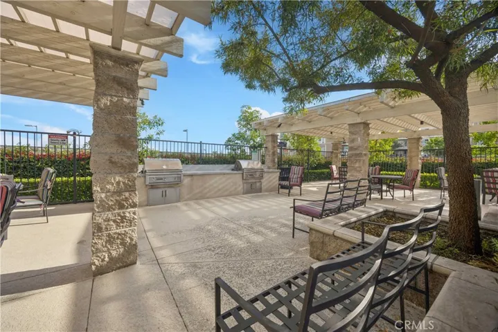 Community outdoor BBQ and lounge area with stone pergola, built-in grills & shaded gathering space.