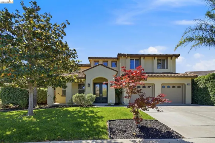 Stucco exterior home featuring a terracotta tile roof, arched entryway, double front doors, and a two-car garage