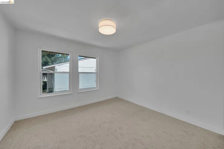 Bright room featuring two windows, neutral carpeting, white walls, white baseboards, and a contemporary flush-mount ceiling light