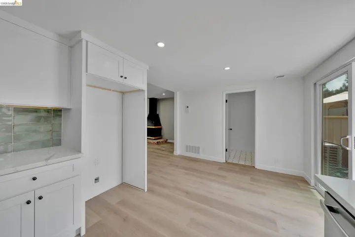 White shaker cabinetry with dark hardware, a refrigerator alcove, and a green tile backsplash
