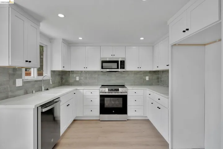 U-shaped kitchen featuring white shaker cabinetry, light-toned countertops, and a gray subway tile backsplash