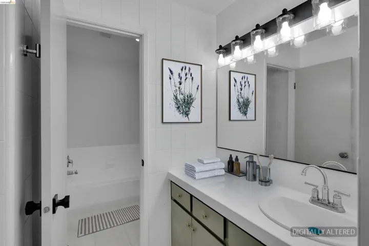 White tiled bathroom featuring a vanity with integrated sink, chrome faucet, and a large mirror