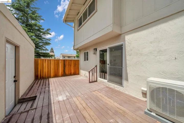 Private outdoor patio featuring wood-finish decking, a sliding glass door, a wooden fence, and a side entrance
