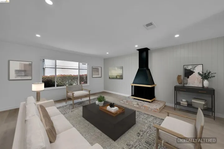 Spacious living area featuring a prominent black range hood style fireplace with a brick hearth, recessed lighting, wood-finish flooring, and a large multi-pane window