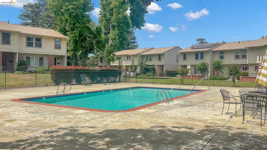 Inviting swimming pool with concrete decking, surrounded by a metal fence and mature trees