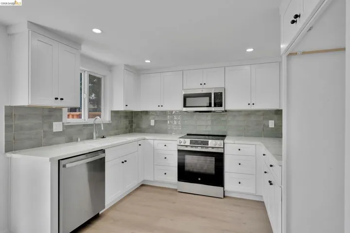 Modern kitchen featuring white shaker cabinetry, stainless steel appliances, a light-toned countertop, and a gray subway tile backsplash