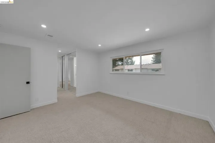 Spacious room featuring neutral carpet flooring, recessed lighting, and a window with a white frame