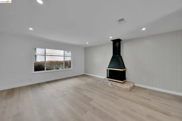 Spacious room featuring wood-finish flooring, recessed lighting, and a modern black fireplace with a brick hearth