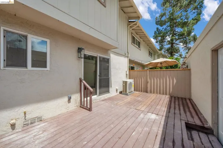 Private outdoor deck area featuring a sliding glass door entry, exterior wall sconce, and perimeter fencing