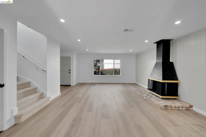Spacious living area featuring light wood-finish flooring, recessed lighting, and a prominent black fireplace with a brick hearth