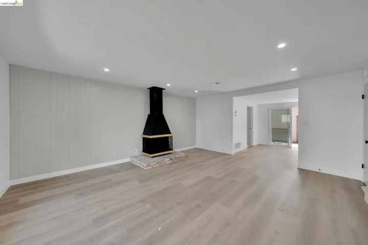 Spacious interior featuring wood-finish flooring, a contemporary black fireplace with a brick hearth, recessed ceiling lighting, and a shiplap accent wall